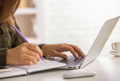 Someone writing in a notebook and typing on a computer