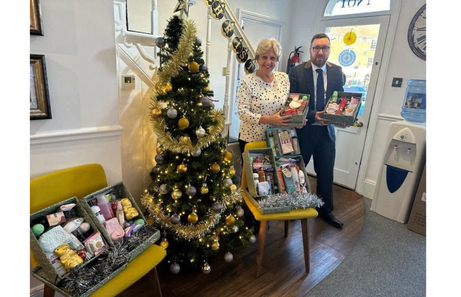 Two people holding a box of donations in front of a Christmas tree