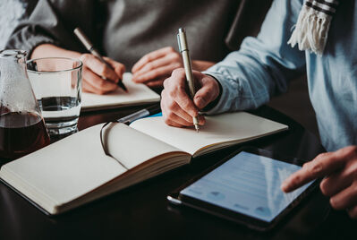 Two people writing in notebooks