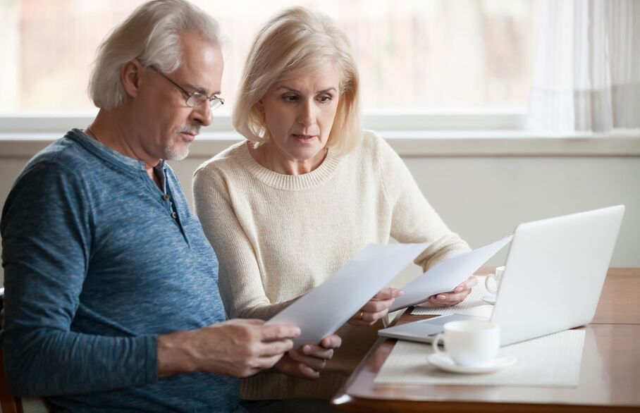 Two people looking at a piece of paper in front of a laptop