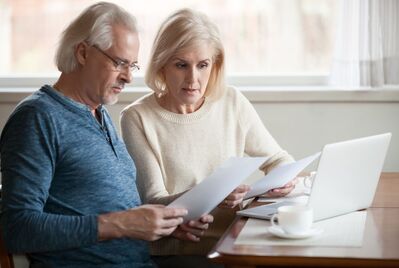 Two people looking at a piece of paper in front of a laptop