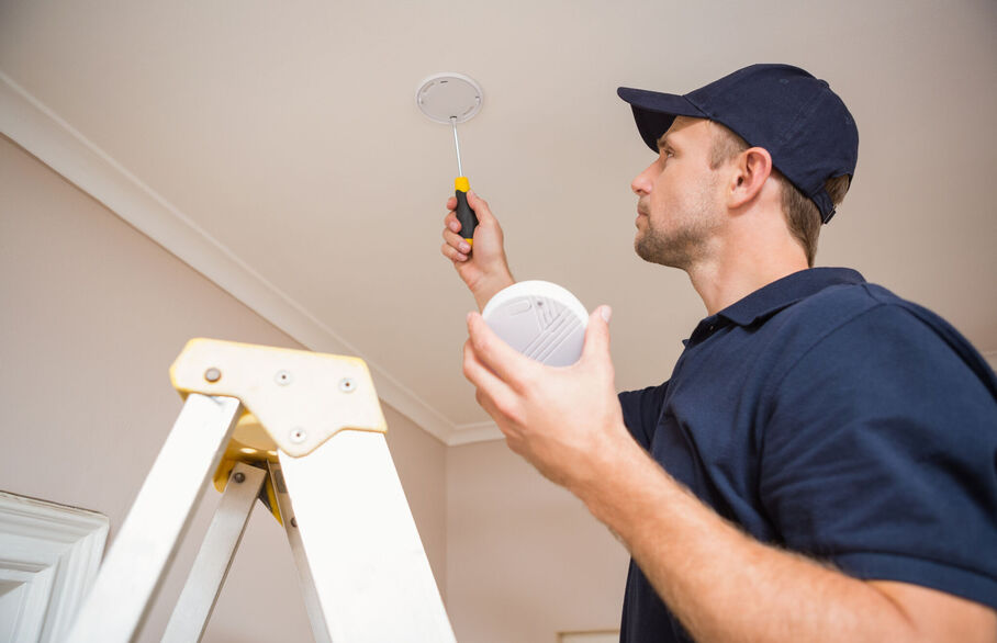 Someone fixing a carbon monoxide detector onto the ceiling