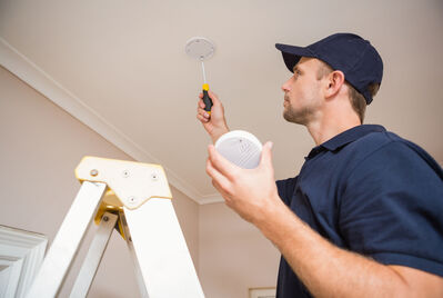 Someone fixing a carbon monoxide detector onto the ceiling