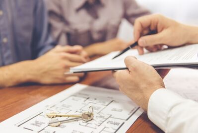 Someone pointing at a clipboard with a house floorplan and pair of keys beneath