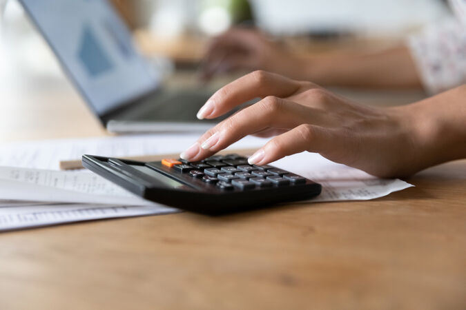 Someone using a calculator and typing on a laptop