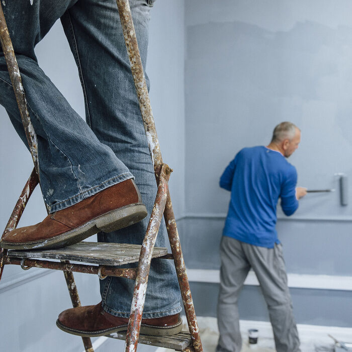 Two male builders are painting a room. 