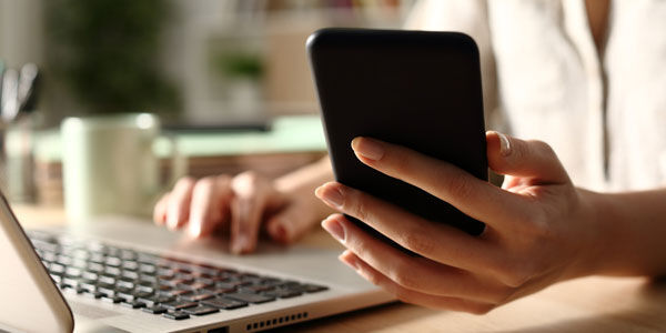 Woman looking at phone whilst on laptop 