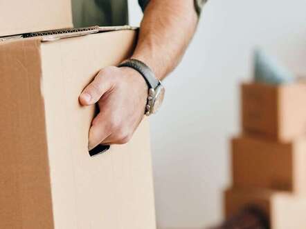 A person carrying a cardboard box with other boxes in the background