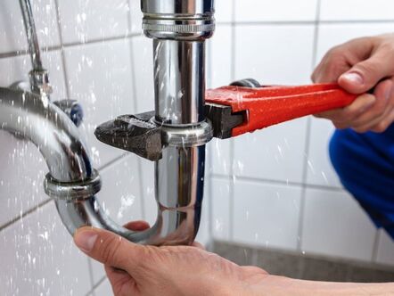 A person fixing a leaking pipe with a tool